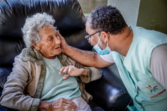Homem usando máscara acaricia rosto de senhora em cadeira de rodas
