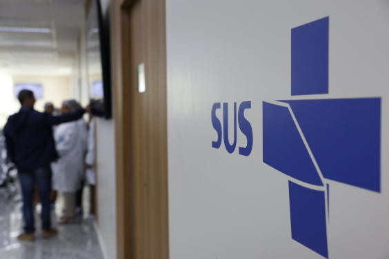 Imagem de corredor de unidade de saúde, com a inscrição SUS na parede