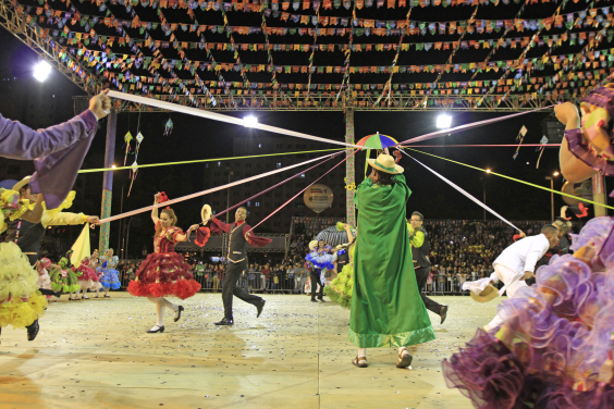 Grupo junino dançando com bandeiras ao fundo no Arraial de Belo Horizonte