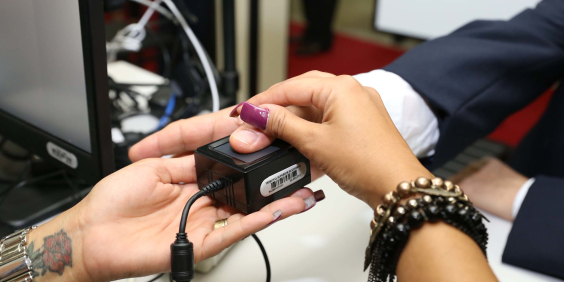 Mãos sobre dispositivo que faz cadastro de biometria