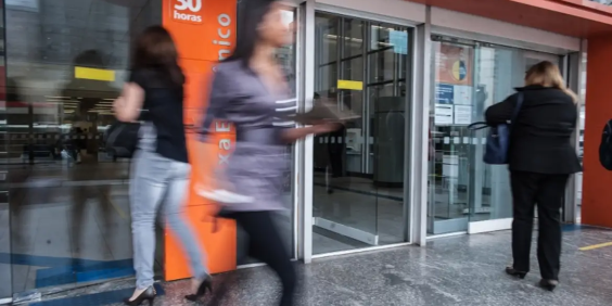 fachada de agência bancária, com pessoas entrando e saindo do estabelecimento