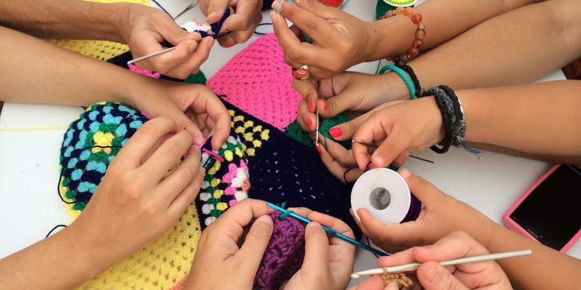 Várias mãos trabalhando juntas na confecção de um peça de crochê