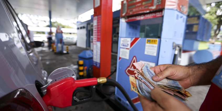 Frentista contando dinheiro em frente a uma bomba de gasolina