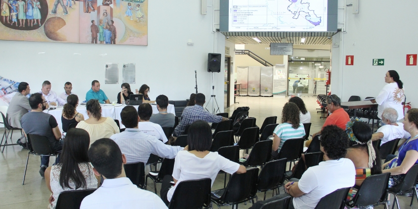 Parlamentares compõem mesa de reunião. Público ocupa cadeira a frente. Painel mostra mapa da região metropolitana de BH