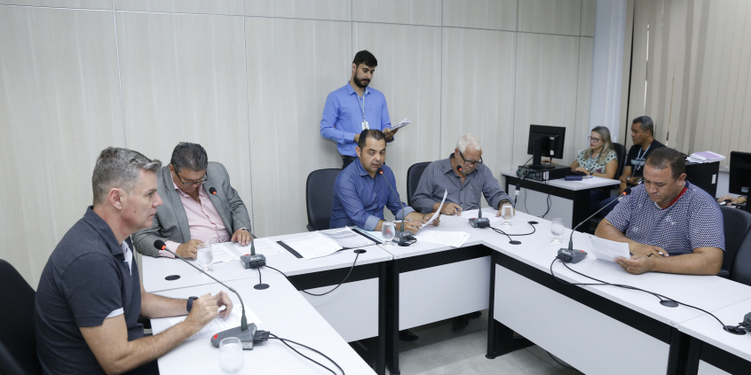 Os cinco integrantes titulares da comissão estão sentados à Mesa, e um coordenador do Processo Legislativo está de pé atrás deles.