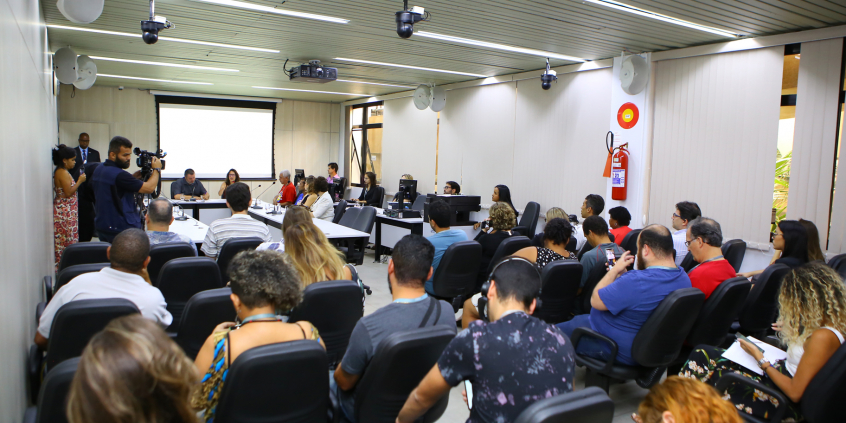 Plenário cheio; público de costas em primeiro plano; vereadores e convidados compõem mesa ao fundo