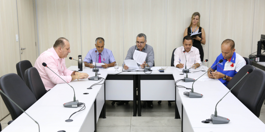 Integrantes da Comissão estão sentados à Mesa apreciando a pauta da reunião. Atrás deles, de pé, uma servidora do Legislativo assessora a reunião