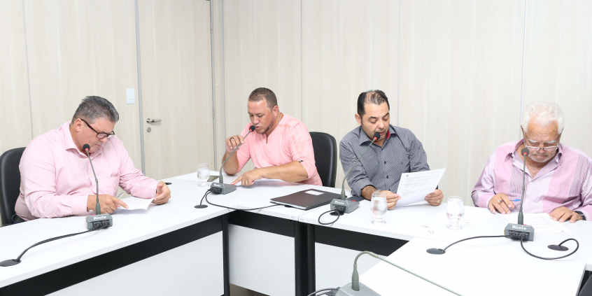 Quatro integrantes da Comissão estão sentados em trono da Mesa, diante de microfones e papéis, apreciando a pauta da reuniãodeles, microfones e 