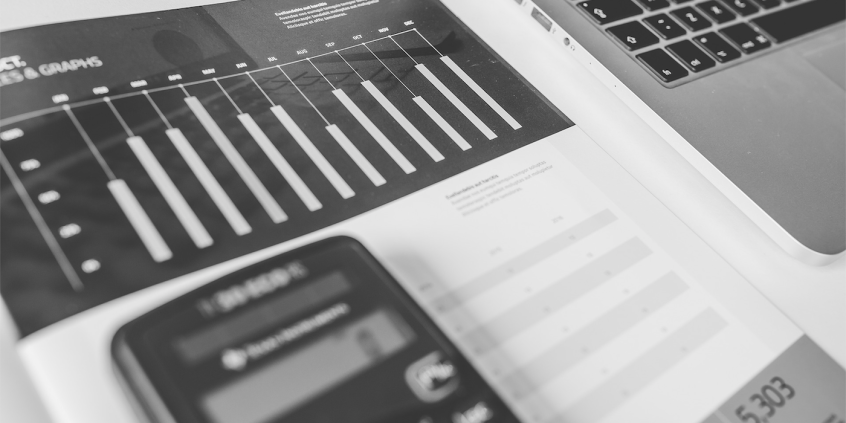 calculadora sobre papel exibindo gráfico de execução financeira mensal. Notebook ao lado