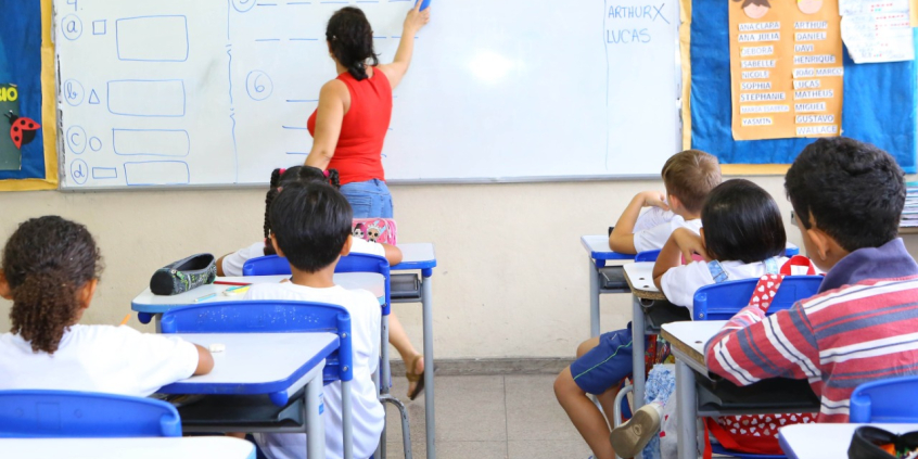 sala de aula da educação infantil. alunos ocupam seus lugares. Professora escreve no quadro.