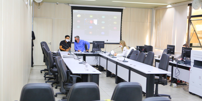 Três parlamentares reunidos no plenário. Os três usam máscaras. Ao fundo, tela em videoconferencia