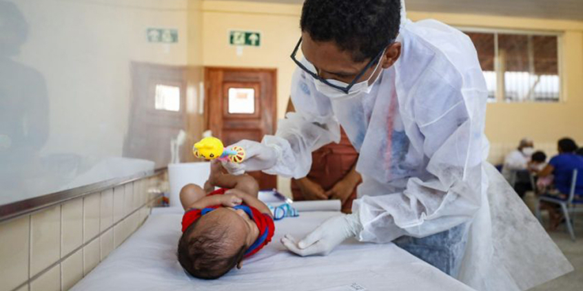 Pediatra atende bebê deitado em cama.