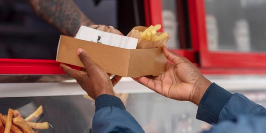 Vendedor entrega lanche para cliente em uma caixa de papel 