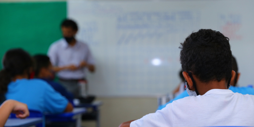 Criança, se costas e de máscara, afastada das outras.  crianças, assiste à aula