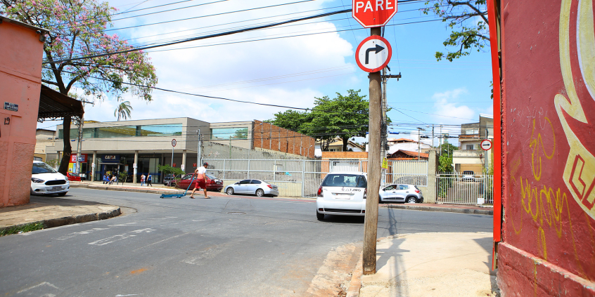 Imagem de um cruzamento de vias com a sinalização horizontal apagada. A sinalização vertical indica parada obrigatória