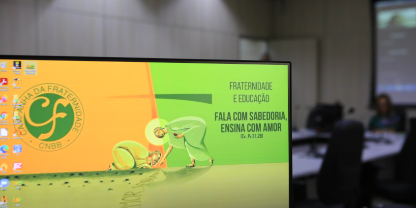 Na tela de um computador, ilustração com a imagem de Jesus Cristo escrevendo no chão as palavras "amor"e "sabedoria", acompanhado por uma pessoa ajoelhada. 