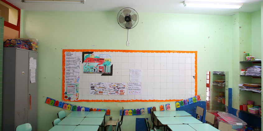 Sala de aula com carteiras enfileiradas. Ao fundo, o quadro branco. A sala está vazia 
