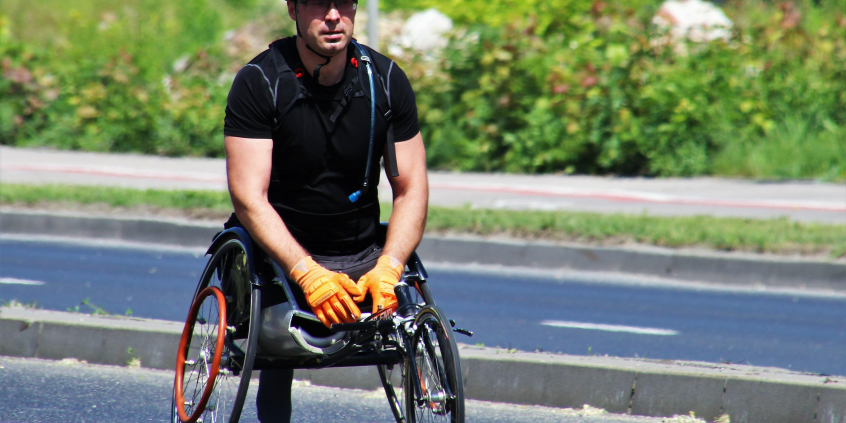 cadeirante do sexo masculino com camiseta e capacete preto e luvas amarelas transitando na rua