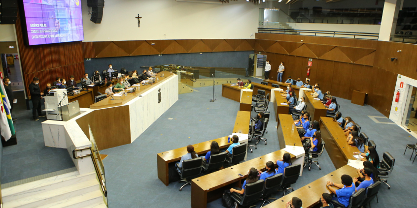 Plenário visto do alto. É possível ver a mesa com os vereadores e as cadeiras ocupadas por adolescentes que participaram da audiência