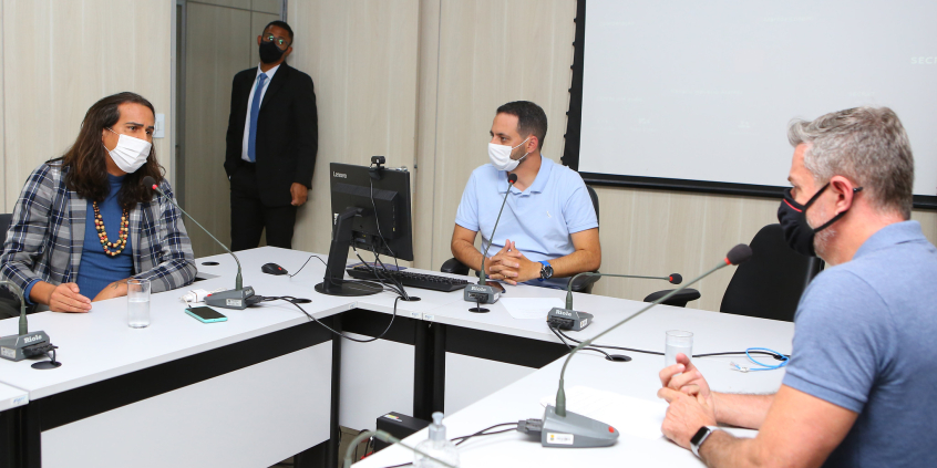 Dois vereadores e uma vereadora sentados à mesa em reunião.