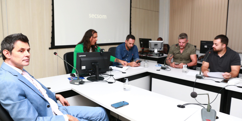 Quatro homens e uma mulher reunidos, sentados à mesa.