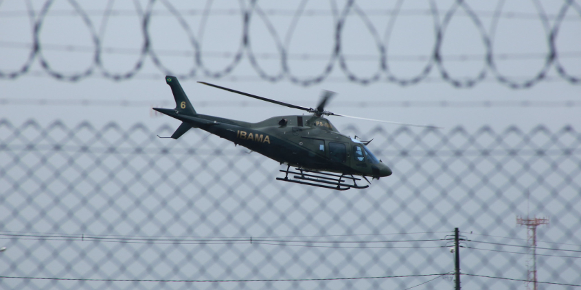 Imagem de um helicóptero no ar. é possível ver a cerca de segurança no local