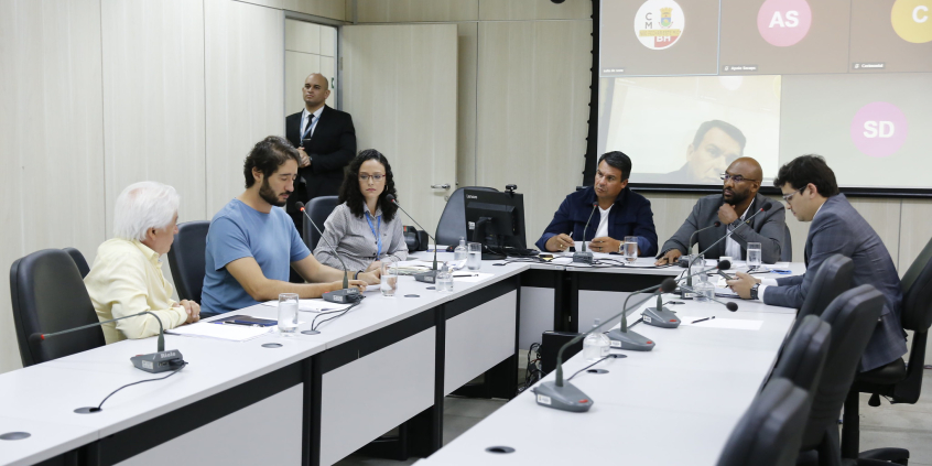 Participantes da reunião sentados em uma mesa em formato de U.
