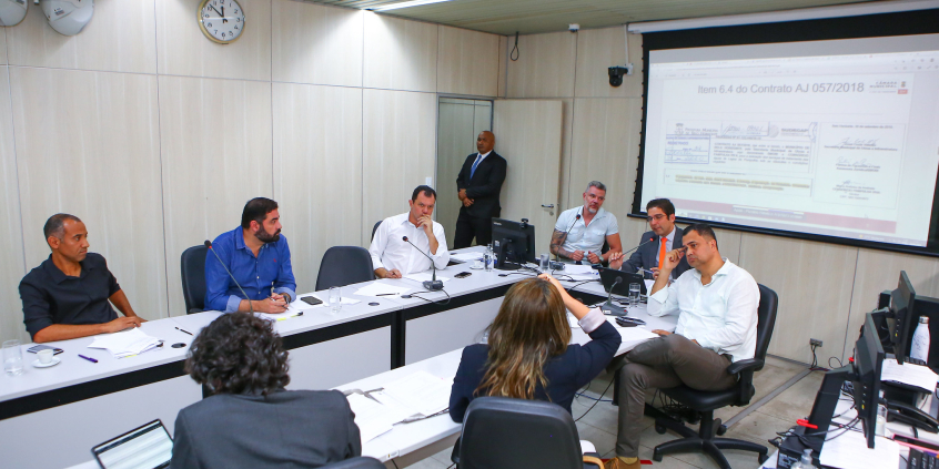 Imagem de participantes em torno da mesa. 