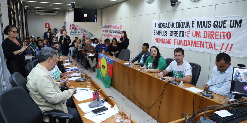 Imagem do Plenário Camil Caram lotado de participantes. Nas paredes , faixas com palavras de ordem e em defesa da moradia digna