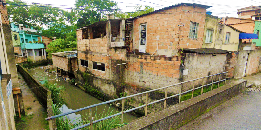 Córrego embiras com lixo em suas águas e rodeado por casas.