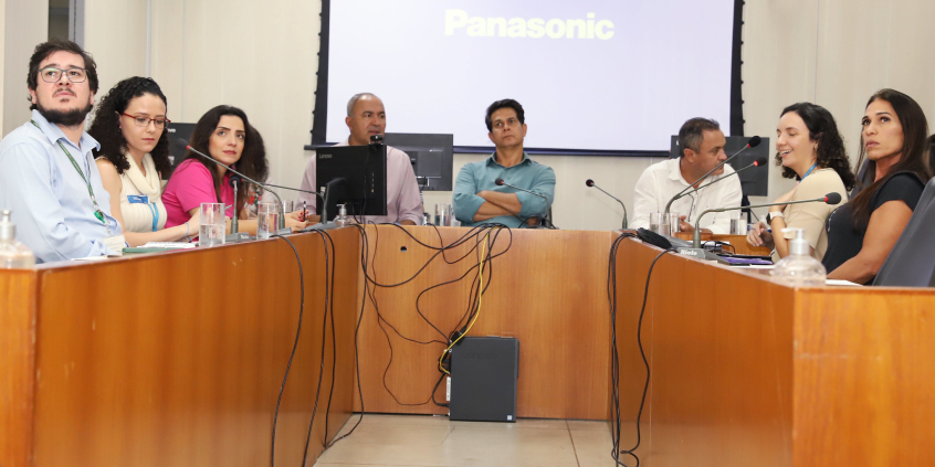 Imagem dos participantes da reunião sentados em uma mesa em formato U 