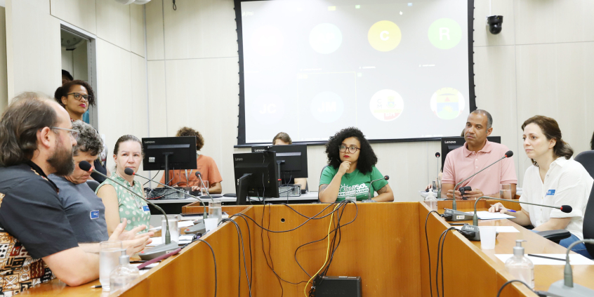 Três mulheres e três homens, sentados, em reunião.