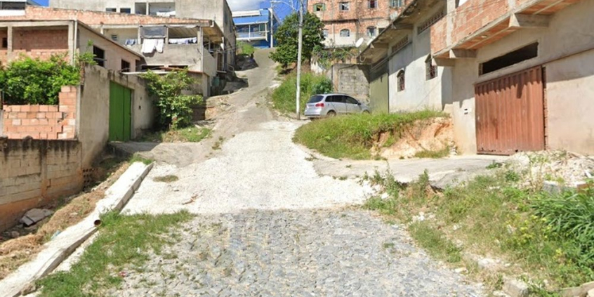 Rua sem calçadas e pavimentação irregular durante o dia.