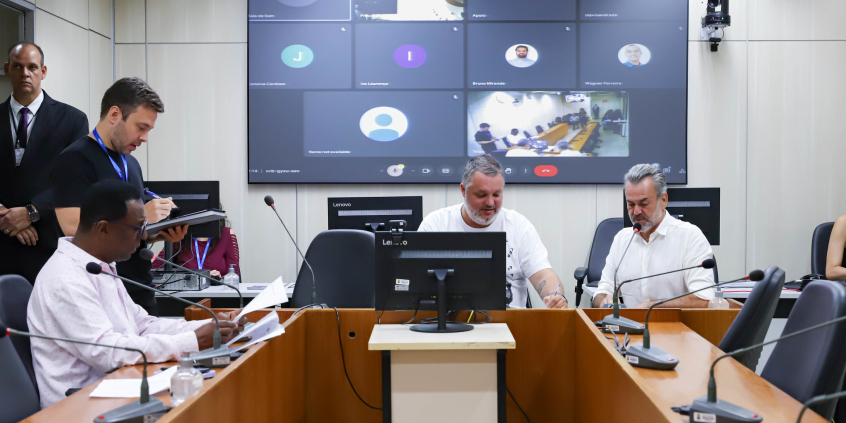 Imagem dos parlamentares Pedro Patrus, Wilsinho da Tabu e Gilson Reis  em torno da mesa em formato de U, durante a reunião. 