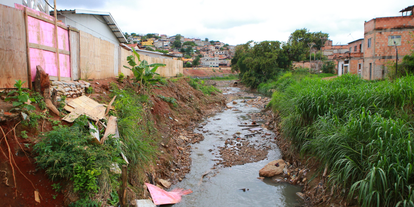 vista de córrego com despejo de resíduos em ambiente urbano