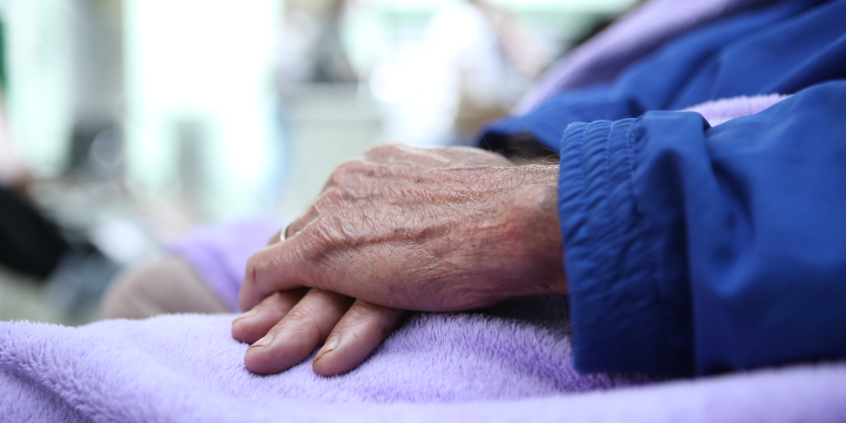 Mãos de pessoa idosa, posicionadas uma em cima da outra sobre um cobertor