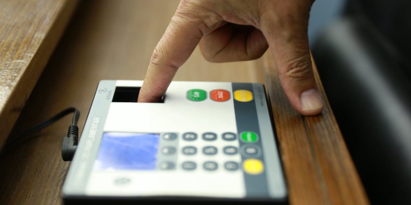 Mão fazendo leitura biométrica de digital em equipamento de votação