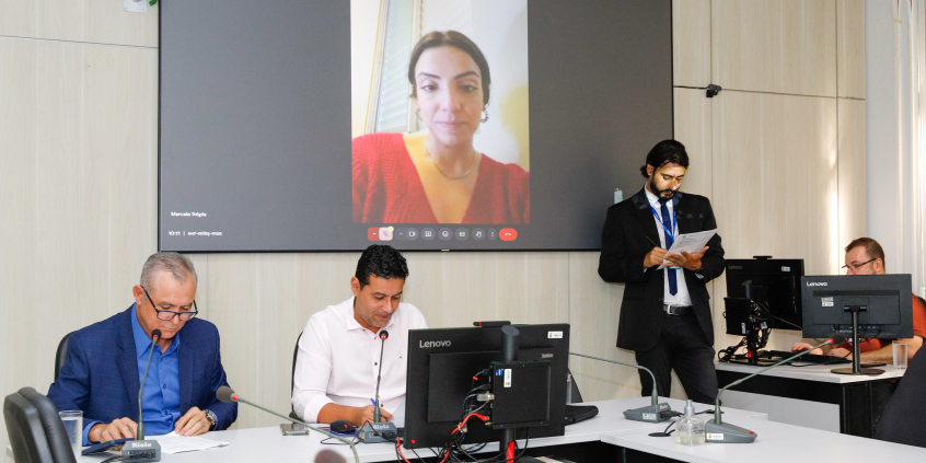 Vereadores no Plenário Helvécio Arantes; a tela atrás deles mostra vereadores presentes virtualmente