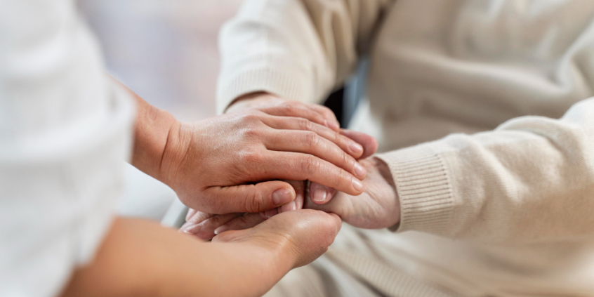 Mãos de pessoa jovem segurando mãos de idosa