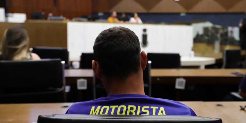 Vista de costas de homem sentado no plenário amintas de barros participando do seminário. Na camiseta dele está escrito "Motorista"