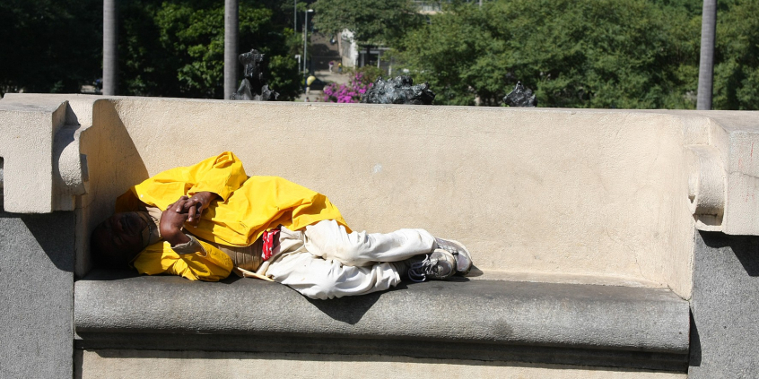 Pessoa em situação de rua deitada em banco
