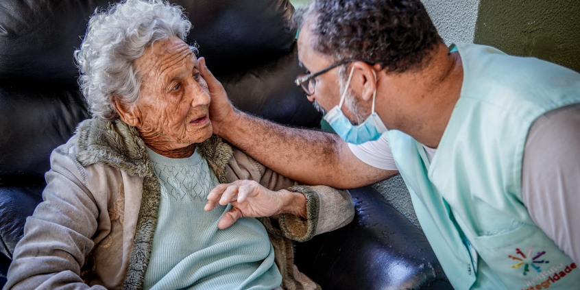 Homem usando máscara acaricia rosto de senhora em cadeira de rodas