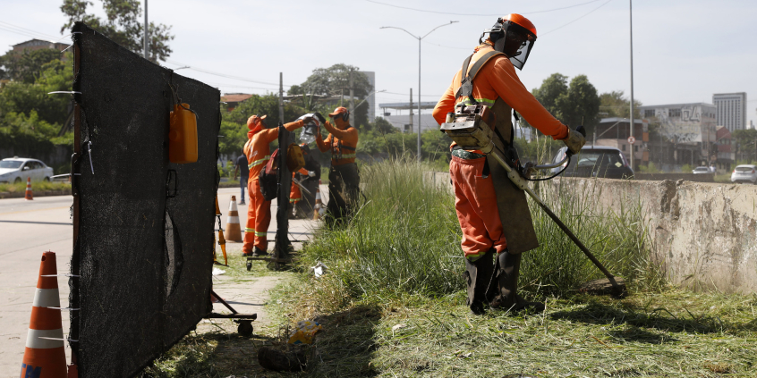 Funcionário da prefeitura capina área de mato em rua da cidade utilizando máquina