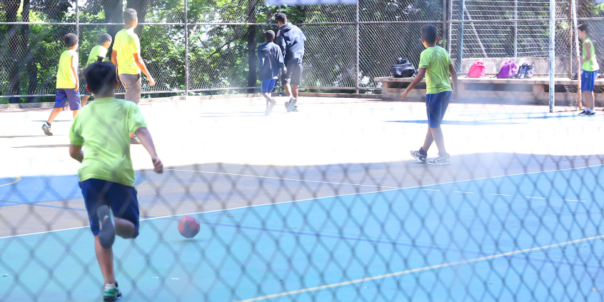 crianças com uniforme de escola brincam com bola em quadra esportiva
