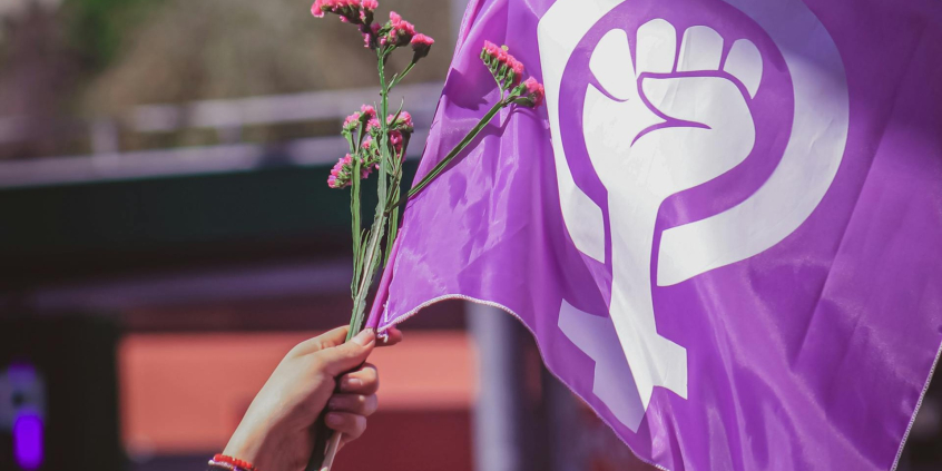 mãos hasteiam bandeira com símbolo do fim da violência contra a mulher