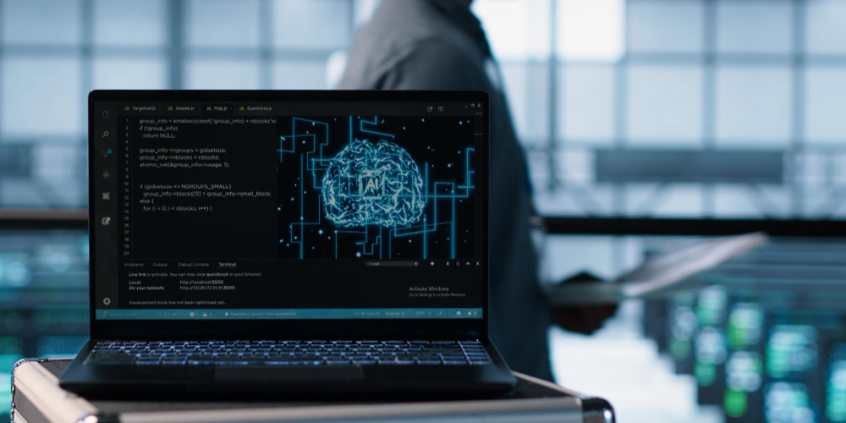 Computador em primeiro plano, com pessoa passando atrás