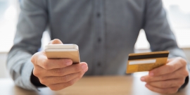 homem segura telefone e cartão de crédito