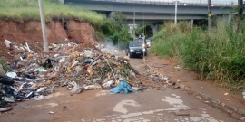 acúmulo de lixo ocupa trecho da via, sob viaduto. Carros desviam.