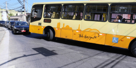 ônibus tem dificuldade de fazer conversão em via de mão dupla em razão da presença de veículos no sentido contrário. Fila de carros se forma para aguardar a manobra do ônibus