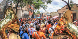 bloco de rua, foliões caminham pela rua, instrumentos de sopro em destaque